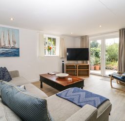 A living room with a gray sofa blue cushions wooden coffee table flat screen TV and a chair near patio doors at The Holt in Harcombe near Sidford