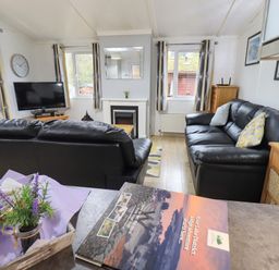 A living room with two black leather sofas a television on a wooden stand and a fireplace at Lavender Lodge in Applethwaite 4 Limefitt Park near Windermere