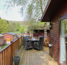 A wooden balcony with a table and four chairs overlooking trees and nearby cabins at Lavender Lodge Applethwaite 4 Limefitt Park near Windermere