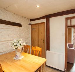A dining area with a wooden table and chairs a vase with flowers on the table and a door leading to a living room at Rustic Cottage in Bowness-On-Windermere