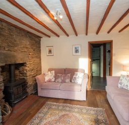 A living room with two pink sofas a stone fireplace a rug and exposed wooden beams at Rustic Cottage in Bowness-On-Windermere