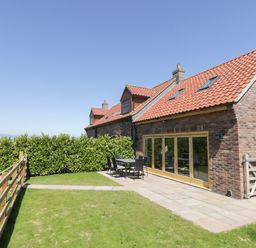 An outdoor patio area with a table and chairs next to a brick house with large windows at Kaitkyella Lodge in Scarborough