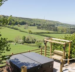 An outdoor patio with a covered hot tub and wooden swing overlooking green fields and hills at Kaitkyella Lodge in Scarborough