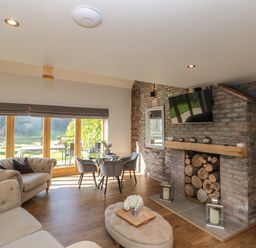 A living room with large glass doors a table with chairs a fireplace with stacked logs and a mounted tv at Kaitkyella Lodge in Scarborough