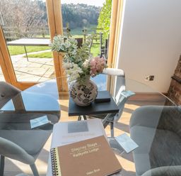 A glass dining table with a vase of flowers and a visitor book on it in a room with grey chairs at Kaitkyella Lodge in Scarborough