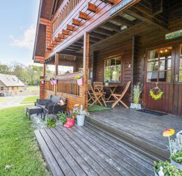A wooden porch with chairs tables flower pots and a wreath on the door at Sun View Lodge in Llanbedr