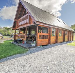 A wooden lodge with a covered porch and outdoor seating on a gravel and grass area at Sun View Lodge in Llanbedr