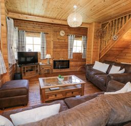 A living room with brown sofas a wooden coffee table a television and wooden walls at Sun View Lodge in Llanbedr