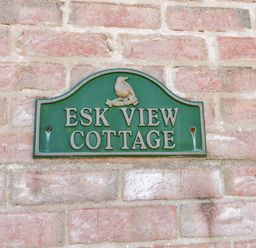 A green sign on a brick wall reading Esk View Cottage at Esk View in Whitby