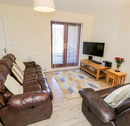 A living room with brown leather sofas a wooden TV stand with a flat screen TV and a side table with flowers at Esk View in Whitby