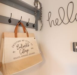 A bag hanging on a wall hook underneath a shelf next to a hello sign on the wall at Bodlondeb in Tremadog