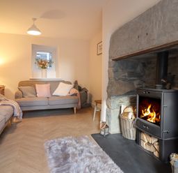 A living room with sofas pillows a small window a lamp and a wood burning stove at Bodlondeb in Tremadog
