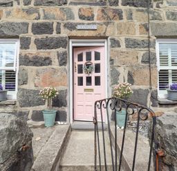 Stone house exterior with a pink door two windows with flower pots and a metal gate at Bodlondeb Tremadog