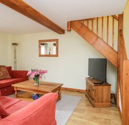 A living room with red sofas a wooden coffee table with flowers a television under wooden stairs at Lavender Cottage in Penruddock