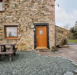 The exterior of a stone building with a wooden door a window a wooden picnic table and a small plant in a pot at Lavender Cottage in Penruddock