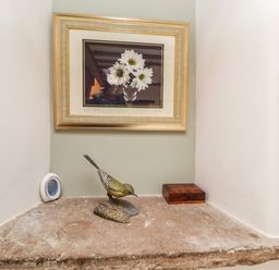 A stone shelf with a bird sculpture a wooden box a small round object and a framed picture of white flowers at Daisy Cottage in Penruddock