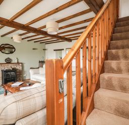 A living room with wooden beams on the ceiling a fireplace a wooden coffee table sofas and carpeted stairs at Daisy Cottage in Penruddock