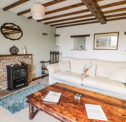 A living room with a beige sofa a wooden coffee table a brick fireplace and exposed wooden beams at Daisy Cottage in Penruddock