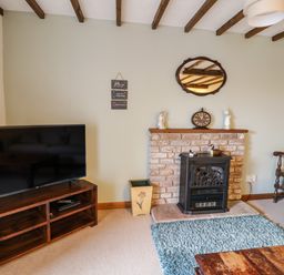 A living room with a television on a wooden stand and a fireplace with a clock and figurines at Daisy Cottage in Penruddock