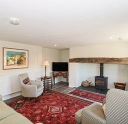 A living room with armchairs a wood burning stove and a red rug at Lilac Cottage in Wookey Hole near Wells