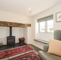 A sitting area with a wood-burning stove baskets a window seat and an armchair at Lilac Cottage in Wookey Hole near Wells
