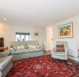 A living room with two armchairs a sofa a red patterned rug table lamps and framed artwork on walls at Lilac Cottage in Wookey Hole near Wells