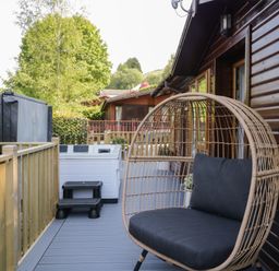 An outdoor deck with a hanging wicker chair and a hot tub at Broad Oak Lodge in Applethwaite 7 Limefitt Park near Windermere