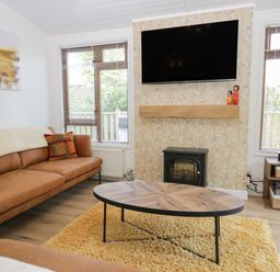 A living room with a brown sofa a wooden coffee table a yellow rug a wall mounted TV and windows at Broad Oak Lodge Applethwaite 7 Limefitt Park near Windermere