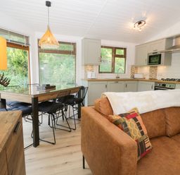 An open plan kitchen and dining area with a brown sofa and a wooden dining table with black chairs at Broad Oak Lodge Applethwaite 7 Limefitt Park near Windermere