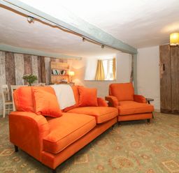 A living room with orange sofa and armchair patterned carpet and rustic wooden door at The Hideaway at Burrow Hill Ottery St Mary