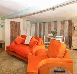 A living room with orange sofas a wooden dining table with chairs and a cabinet at The Hideaway at Burrow Hill Ottery St Mary