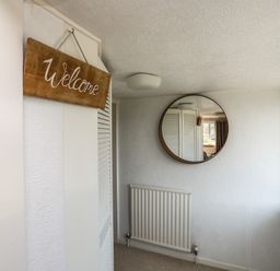 A hallway with a welcome sign a round wall mirror a radiator and a door at Ty Bedw in Benllech