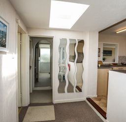 A hallway with three wavy mirrors on the wall and a doorway leading to a kitchen at Ty Bedw in Benllech