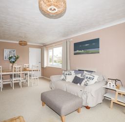 A living room with a sofa and ottoman a dining table with chairs and a television on a stand at Ty Bedw in Benllech