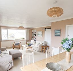 A living room with sofas a coffee table and a dining table with flowers at Ty Bedw in Benllech