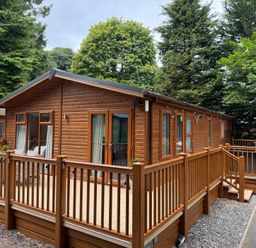 A wooden lodge with a deck and railing at Cherry Tree Lodge, Calgarth 37, White Cross Bay near Windermere