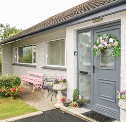 A house entrance with a gray door decorated with a floral wreath pink bench small table with two chairs and flower pots at 27 Pinewood Hill in Warrenpoint Northern Ireland