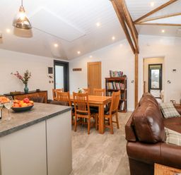 An open living and dining area with a kitchen island bowls of fruit wooden dining table brown leather sofas and bookshelves at Stables Lodge in Wingerworth