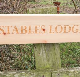 A wooden sign with the text Stables Lodge mounted on a weathered wooden post outdoors at Wingerworth