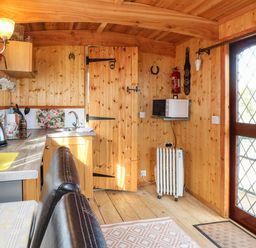 A small wooden kitchen with a toaster kettle and microwave near a door with diamond patterned glass at Packhorse Shepherds Hut Alderwasley near Wirksworth
