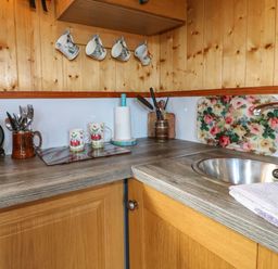 A kitchen corner with wooden cabinets a stainless steel sink a kettle mugs cutlery and paper towels at Packhorse Shepherd's Hut in Alderwasley near Wirksworth