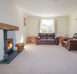 A living room with a fireplace two brown leather sofas and a window with curtains at Ilgram in St Newlyn East