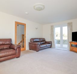 A living room with two brown leather sofas a wooden TV stand with a television and a glass door leading outside at Ilgram in St Newlyn East