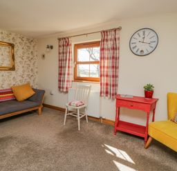 A living room with a gray sofa orange cushion yellow chair red table and white chair by a window at Bramblewood Cottage in Crookdake near Bassenthwaite