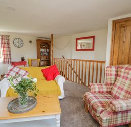 A sitting area with a plaid armchair and sofa with yellow cover a wooden coffee table with flowers and a bookshelf at Bramblewood Cottage in Crookdake near Bassenthwaite