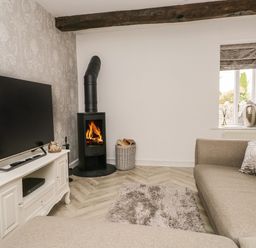 A living room with a sofa a wood burning stove and a television at Bella Cottage Bolton near Appleby-in-Westmorland