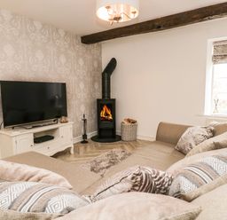 A living room with a television on a white stand and a wood-burning stove at Bella Cottage Bolton near Appleby-in-Westmorland