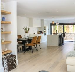 An open plan kitchen and dining area with a dining table and chairs kitchen island with bar stools and large windows at Sail Loft in Dawlish