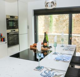 A kitchen with white countertop and black chairs set with placemats glasses and cutlery at Sail Loft in Dawlish