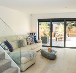 A living room with a beige sofa and glass coffee table near sliding glass doors at Sail Loft in Dawlish
